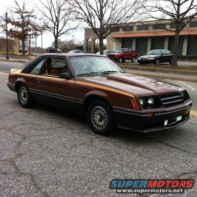 Brown 1980 Ford Mustang with a hood scoop and gold pinstripes parked on a street