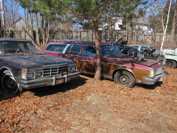 Several old cars parked in a yard, including a wood-paneled station wagon