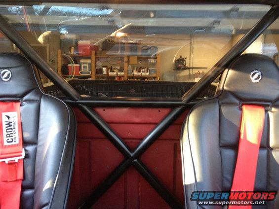 Interior view of racing seats and roll cage in a truck cab. Red racing harnesses visible