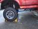 1996 Ford F-150 - Close-up of a red truck's lifted suspension and large tire, with "James Duff" branding on a blue component.