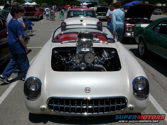 Front view of a white classic car with a large supercharger and V8 engine exposed in the front
