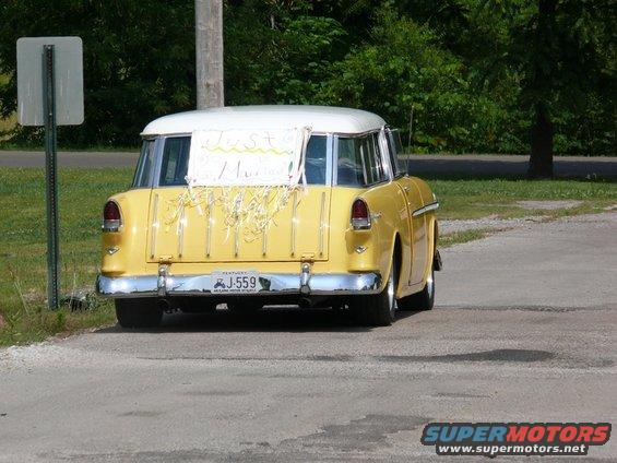 Yellow 1955 station wagon, rear view, with 'Just Married' sign and streamers on the tailgate