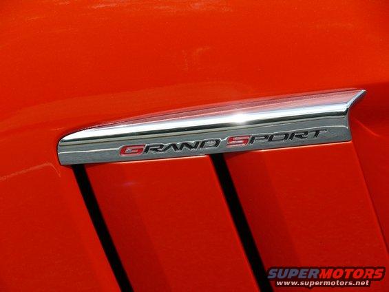 Orange car fender with a chrome trim piece and a red and silver "GRAND SPORT" emblem