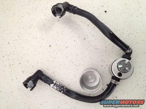 Automotive fuel line with a silver canister and black hoses, laid out on a speckled surface
