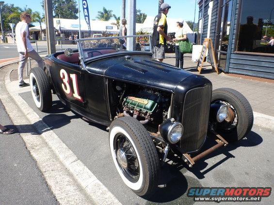 Black hot rod with number 31 on the side, exposed engine, and whitewall tires parked on street