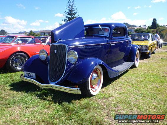 Blue 1933 coupe with hood open, chrome bumper, whitewall tires, parked on grass