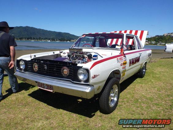 White Dodge Dart drag car with red stripes, open hood showing engine, and red/white striped roof. License plate reads GAS 318I