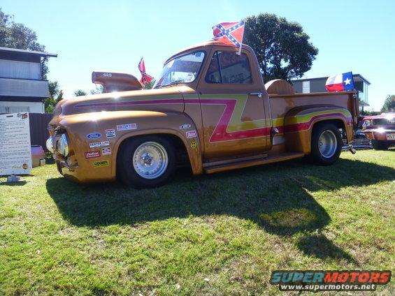 Gold pickup truck with racing decals and a large hood scoop, displaying Confederate and Texas flags