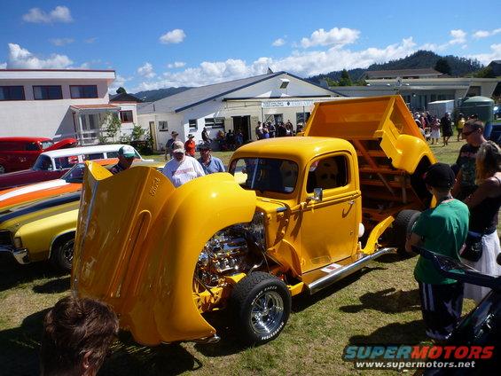 Yellow dump truck with hood open, showing engine and chrome details. Dump bed is raised
