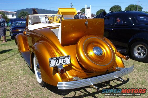 1936 convertible, gold paint, continental kit, white wall tires, chrome bumper, dual exhaust. Black coupe in background