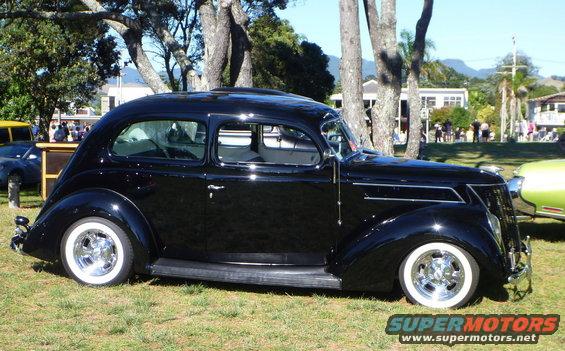 Black sedan with whitewall tires parked on grass, side view