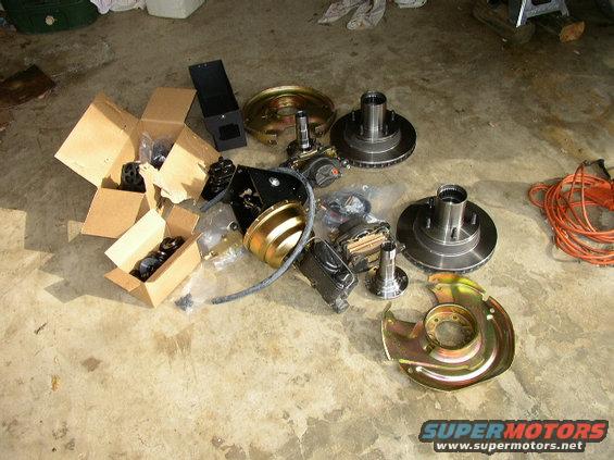 Vehicle brake rotors, hubs, calipers, and boxes of parts on concrete floor