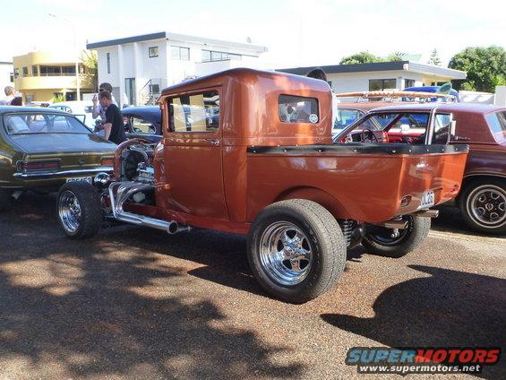 Orange hot rod pickup truck, rear 3/4 view, with exposed engine and chrome pipes
