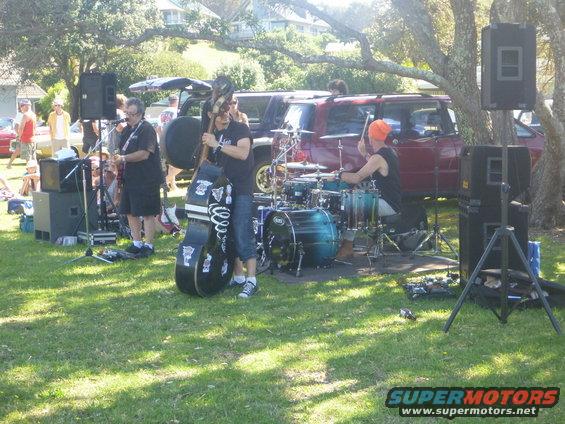 Band performing outdoors with red SUVs parked behind them