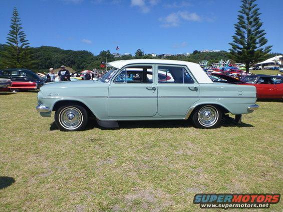 Pale blue sedan with white roof parked on grass, other cars and trees in background
