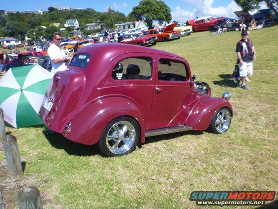 Maroon sedan with chrome wheels parked on grass at an outdoor event