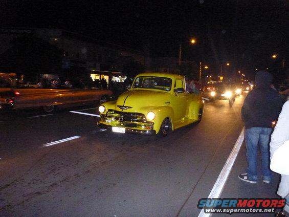 Yellow 1954 Chevrolet pickup truck driving at night, 3q-front view