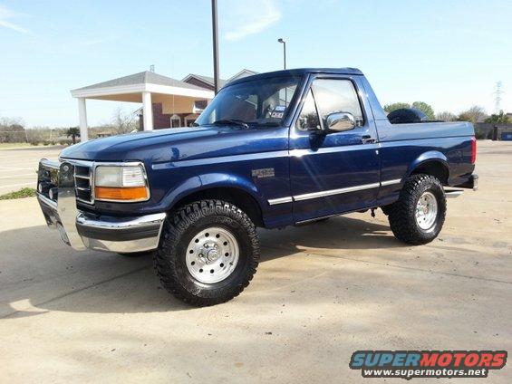 Blue 1995 Ford Bronco with aftermarket chrome bull bar and off-road tires