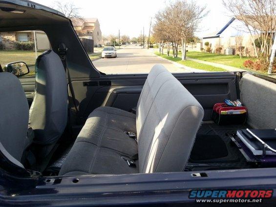 1995 Ford Bronco interior showing front and rear seats, with a street visible through the open top