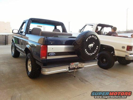 Dark blue Ford Bronco with spare tire cover, parked next to a white pickup truck