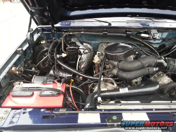1995 Ford Bronco engine bay with blue paint, red battery, and various hoses and components