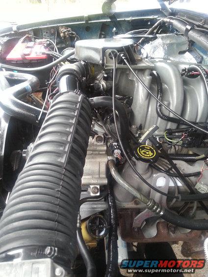 Engine bay with large ribbed air intake hose, battery, and various engine components. Oil cap visible