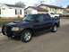 2005 Ford Sport Trac - A dark 2005 Ford Sport Trac is parked on a street in front of houses, with a white pickup truck in the background.