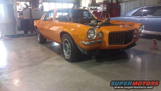 Orange muscle car with hood open, front 3/4 view, in a garage with another car