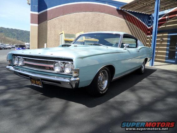Light blue 1970 Ford Torino GT with a hood scoop and chrome grille, parked in front of a building