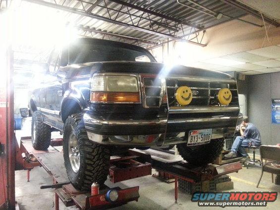 Black 1995 Ford Bronco on a lift, front view, with smiley face lights on the grille