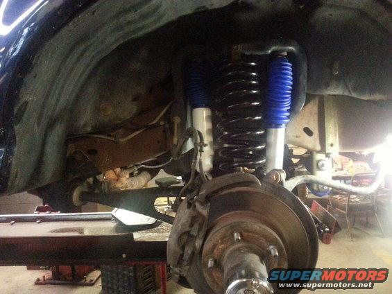 Close-up of a vehicle's front suspension with blue shock absorbers and a large coil spring