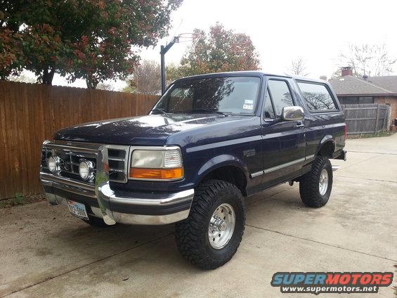 Dark blue Ford Bronco parked on a driveway. It has aftermarket wheels and tires