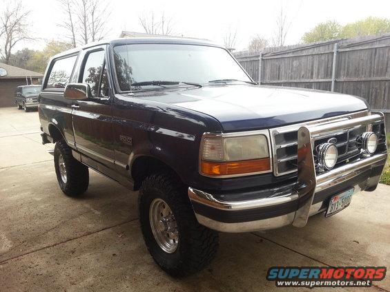 Dark blue Ford Bronco with chrome grille guard and aftermarket wheels parked on a driveway