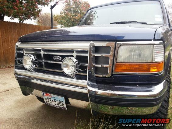 Front of a dark blue Ford F-150 truck, showing the grille with two round fog lights and the Ford logo. License plate reads BY3-5006