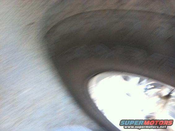 Close-up of a wheel well with a tire visible through the opening. Supermotors.net logo in the corner