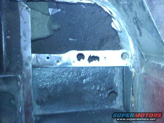 Close-up of a vehicle's frame showing metal bracing and holes, likely during repair work