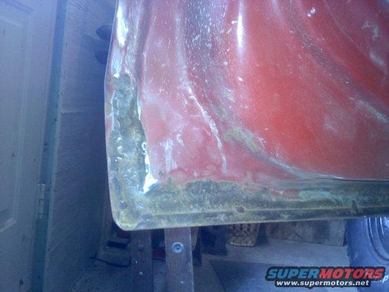 Close-up of a red vehicle's lower body panel showing rust and damage