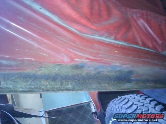 Red interior panel with visible rust and damage along the bottom edge, next to a tire