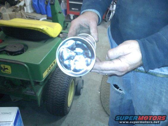 Person holding a clear tube with ice inside, in front of a green John Deere lawn tractor