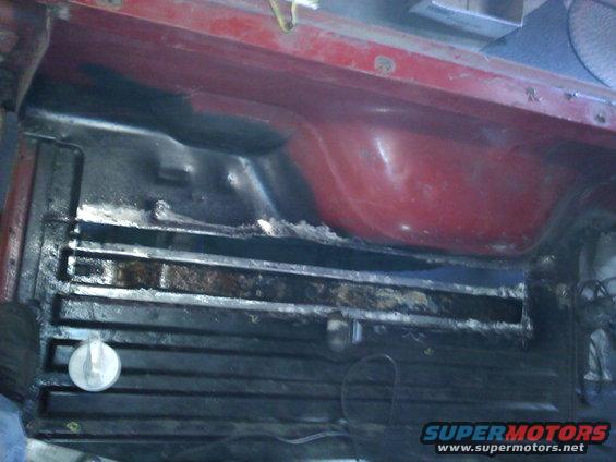Red vehicle cargo area with black textured floor and visible rust on metal supports
