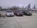 2003 Ford Crown Victoria - Three sedans are parked in a lot near a body of water with a city skyline in the distance.