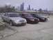 2003 Ford Crown Victoria - Three Ford Crown Victorias are parked in a lot with a city skyline visible behind them.