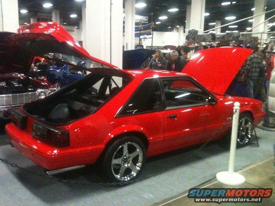 Red 1987 Ford Mustang coupe with hoods open, chrome wheels, at a car show
