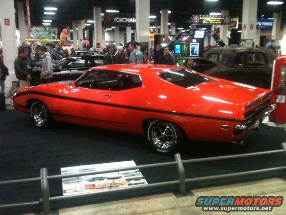 Red 1970s coupe with black racing stripes and chrome wheels