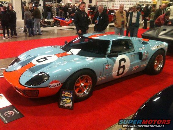 Light blue race car with orange stripes and the number 6 on it, parked on a red carpet