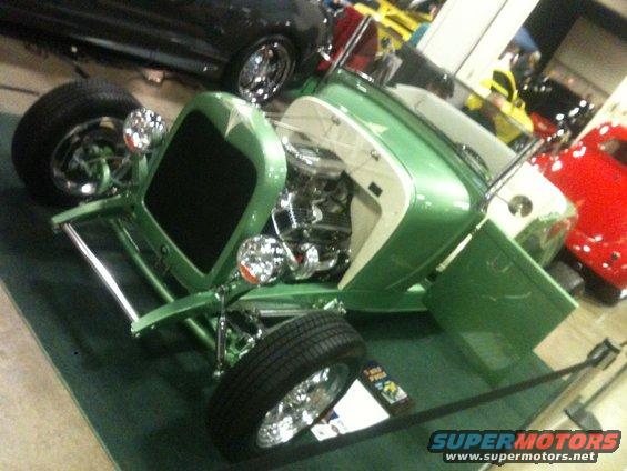 Green hot rod with open door and exposed engine. Other cars visible