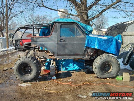 SUV body on a custom frame with large tires, covered in tarps, undergoing modifications