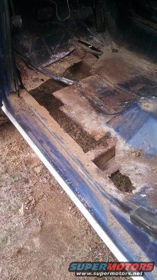 Blue vehicle interior showing severely rusted floor panels and exposed ground beneath