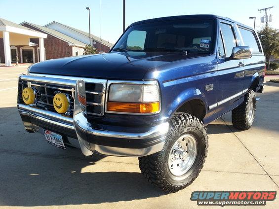 Blue 1995 Ford Bronco with chrome bumper, aftermarket wheels, and two yellow smiley face lights on the grille