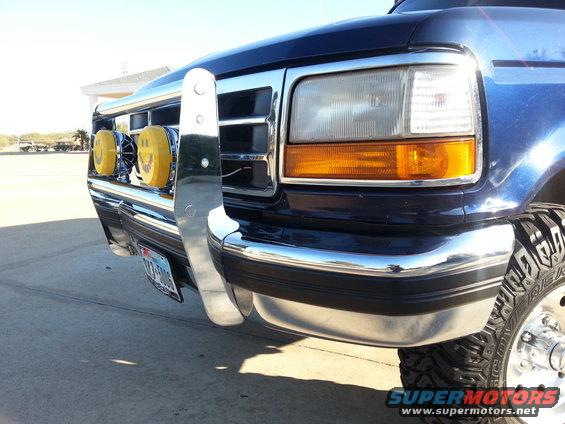 Blue Ford truck front end with chrome bull bar, yellow smiley face lights, and aftermarket tires